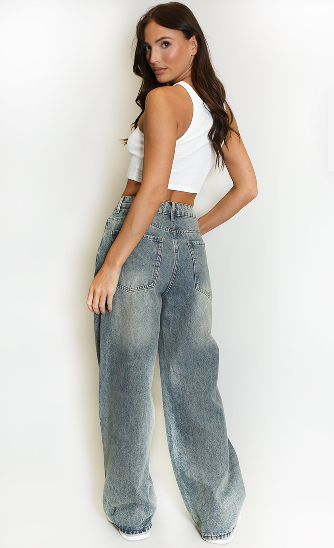 back of Woman wearing a white crop top and blue jeans against