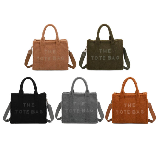 A collection of tote bags in different colours: black, brown, grey, green, and beige, each with a long crossbody strap and embossed detail that reads 'THE TOTE BAG'.