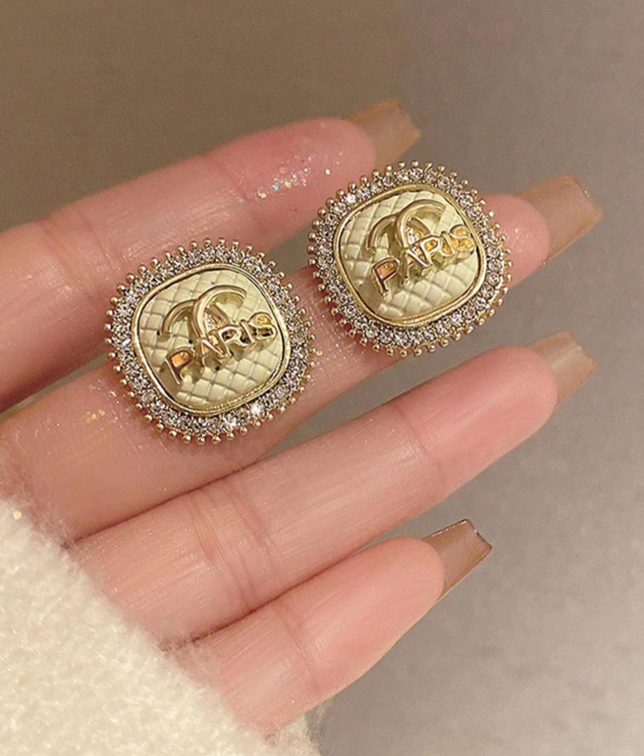Gold and diamond-encrusted earrings held between fingers