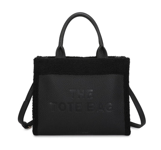 A black tote bag with a fuzzy edge and a long adjustable strap, featuring the text 'THE TOTE BAG' embossed on the front.