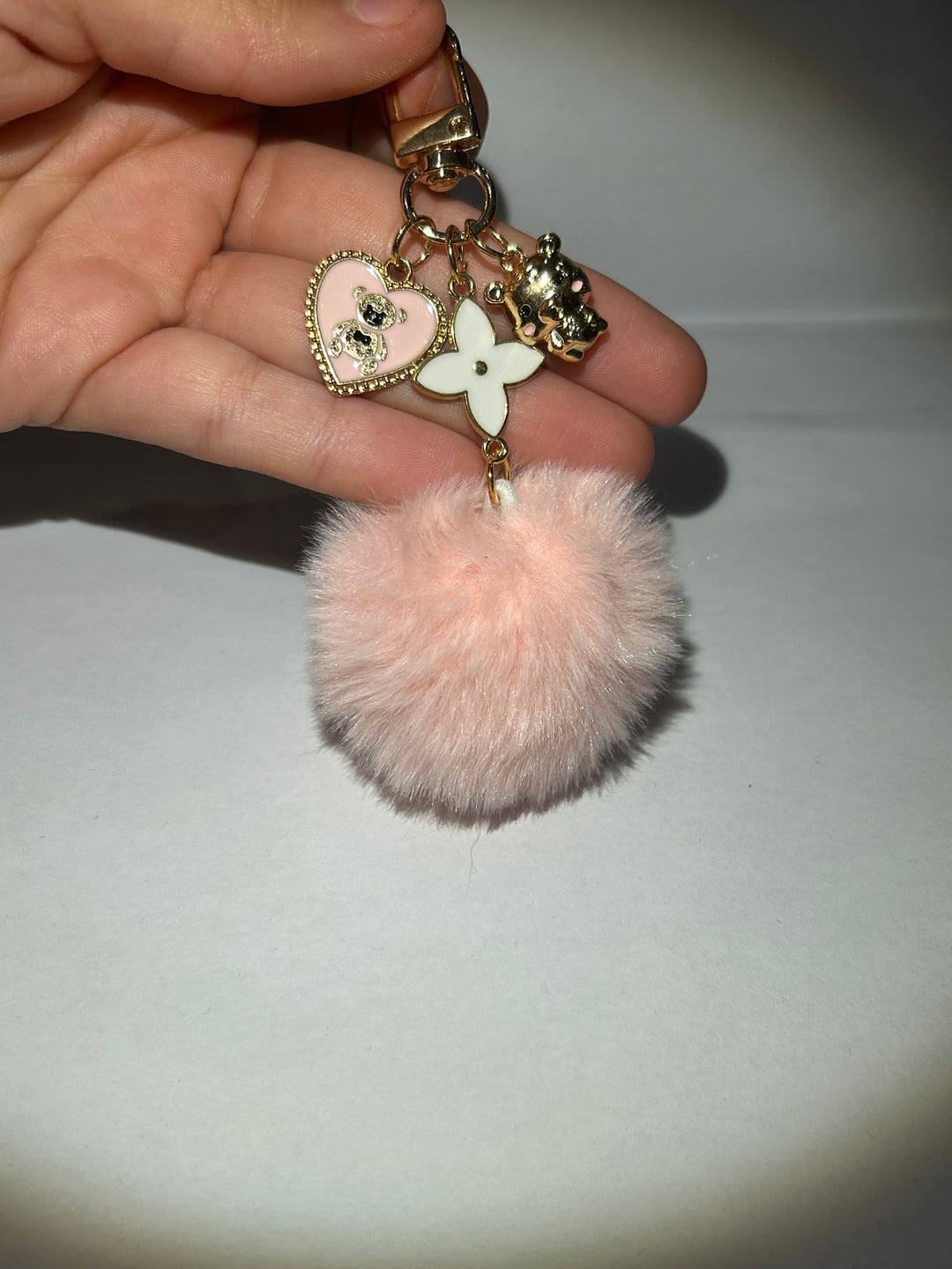 A pink clover flower key ring with a fluffy pom-pom and additional charms attached to it.