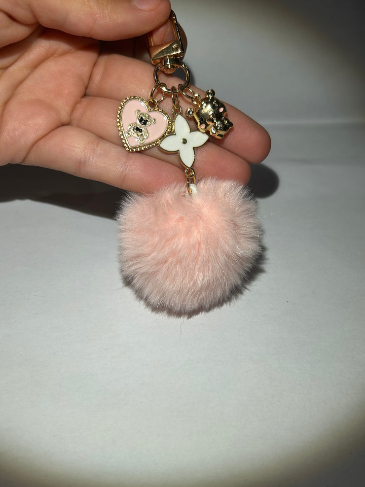 A pink clover flower key ring with a fluffy pom-pom and additional charms attached to it.