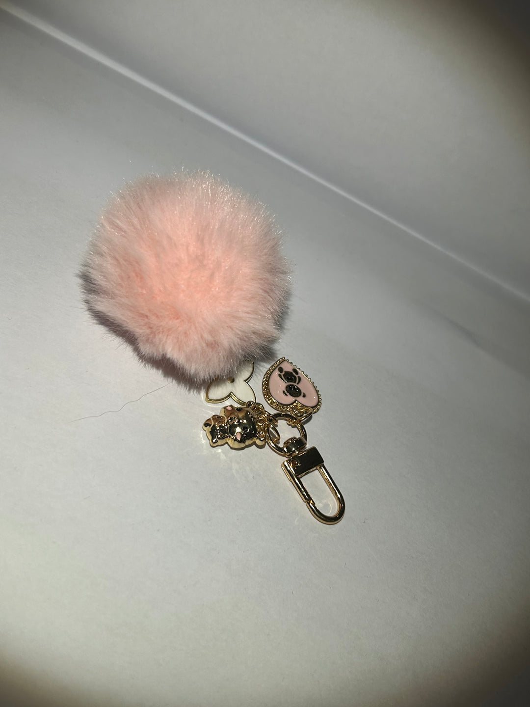 A pink clover flower key ring with a fluffy pom-pom and additional charms attached to it.