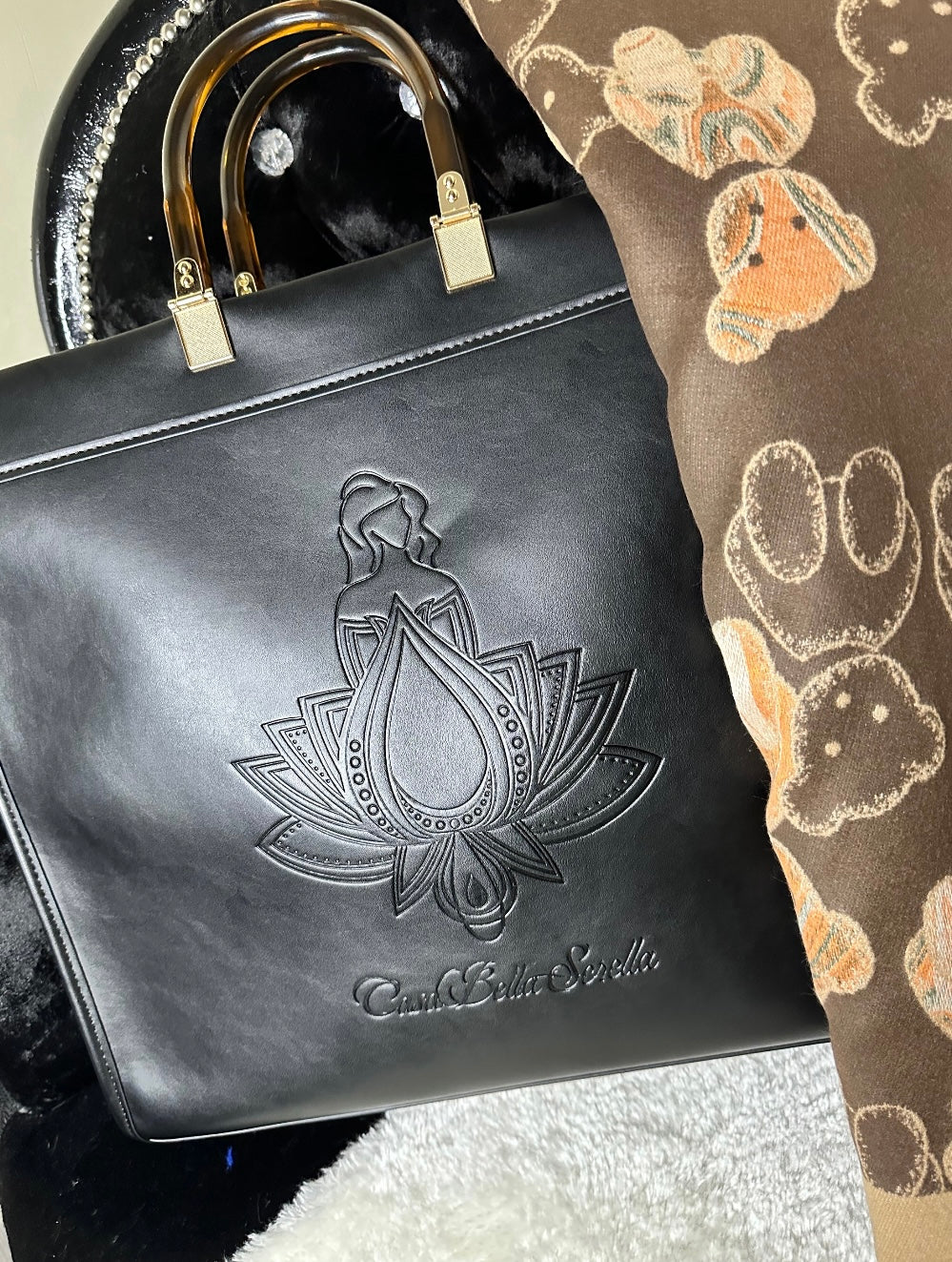 An image showing a black handbag tote with an embossed cbs logo design, and a scarf. 