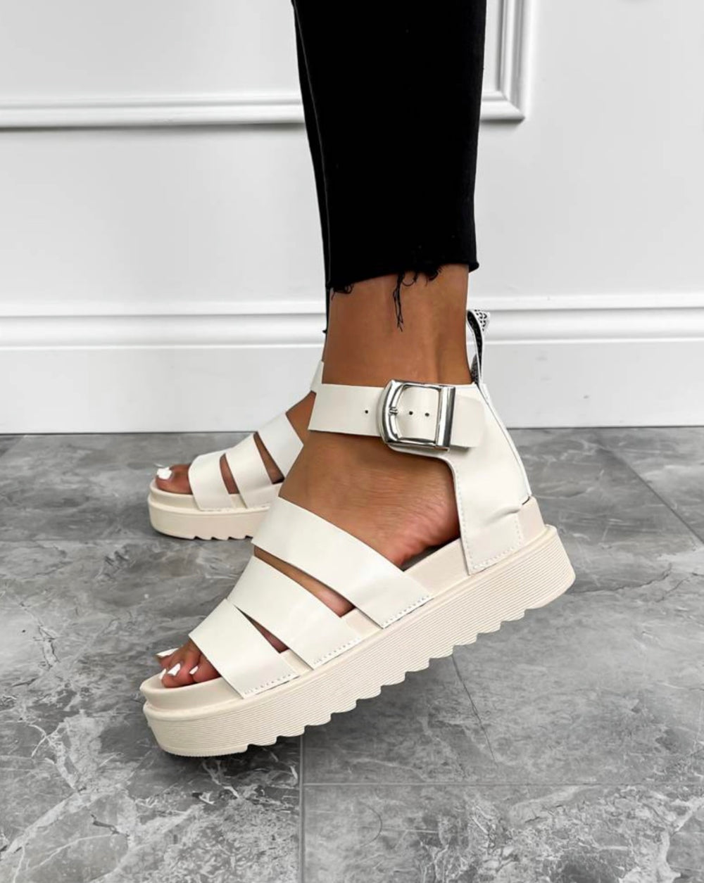 A pair of beige gladiator sandals with a buckle strap