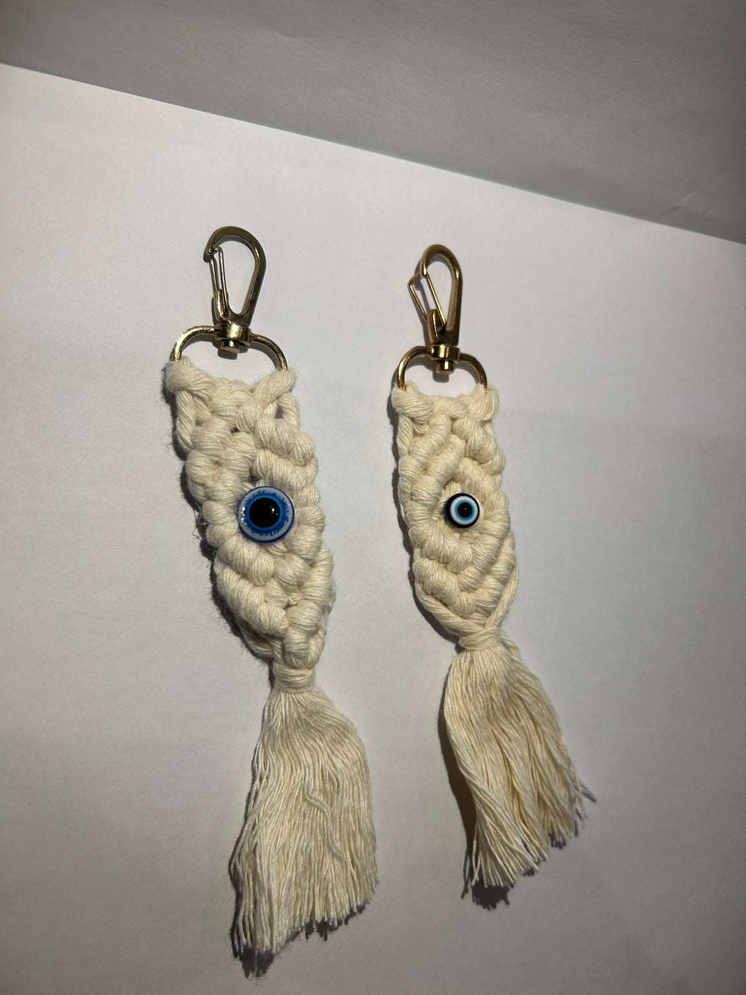 A pair of key rings with a blue eye design, made of a woven beige material