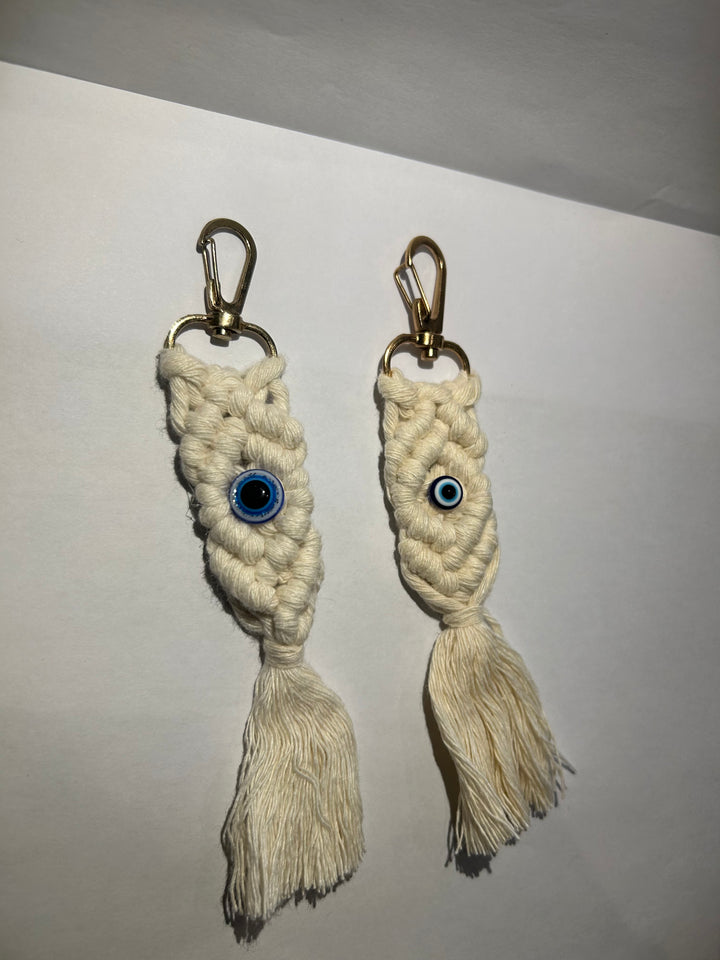 A pair of key rings with a blue eye design, made of a woven beige material