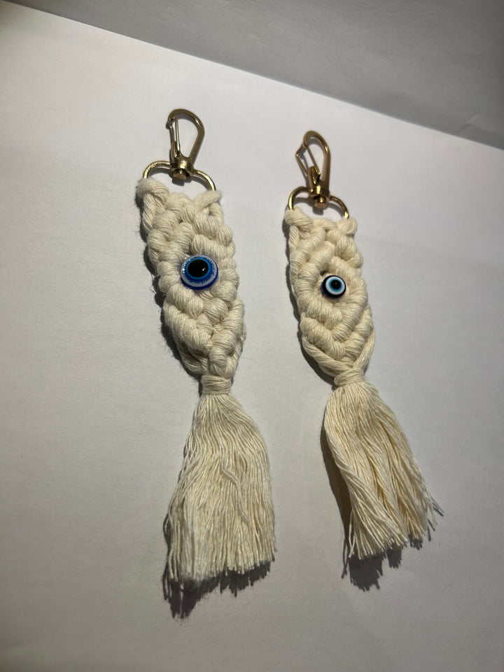 A pair of key rings with a blue eye design, made of a woven beige material