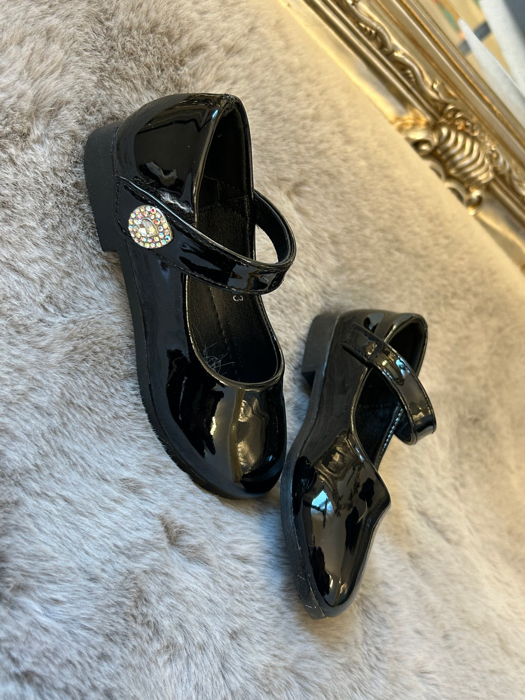 A pair of black, patent leather little girl's school shoes with crystal detailing, 