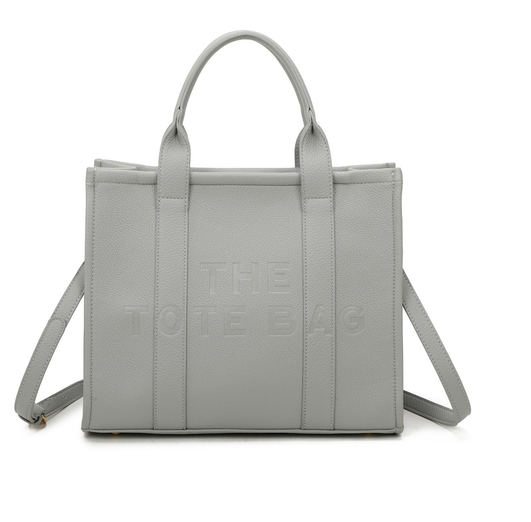 A grey tote bag with embossed ‘The Tote Bag’ text, structured design with top handles and detachable shoulder strap