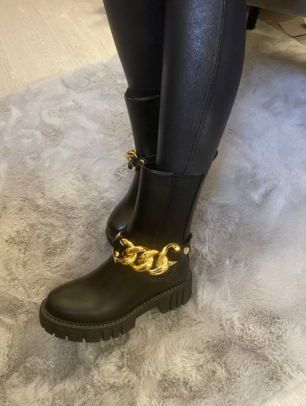 Black chunky ankle boots with gold chain detail worn on feet, stylish women’s boots

