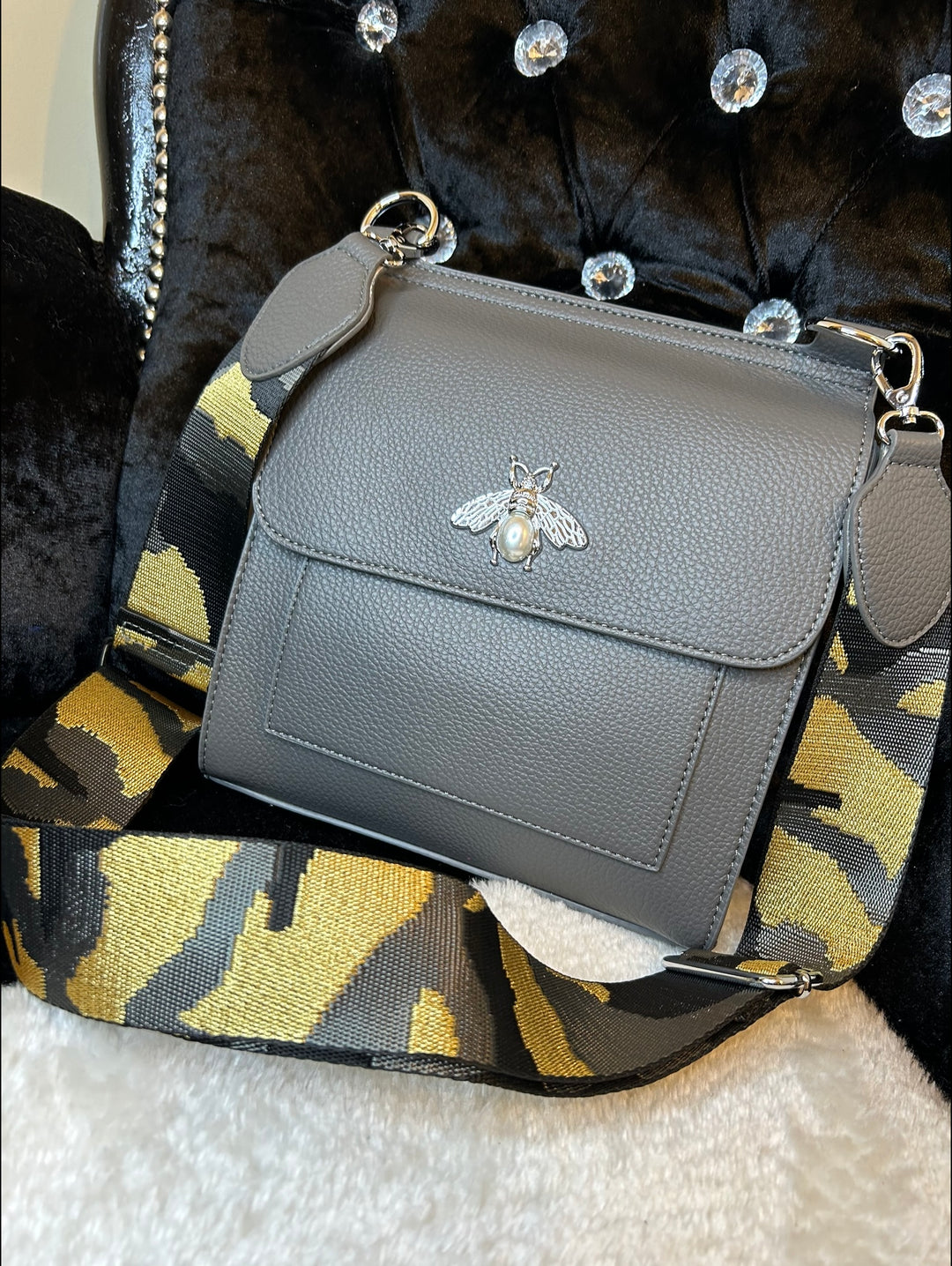 Grey crossbody bag with silver bee and pearl detail on flap, adjustable monochrome patterned straw