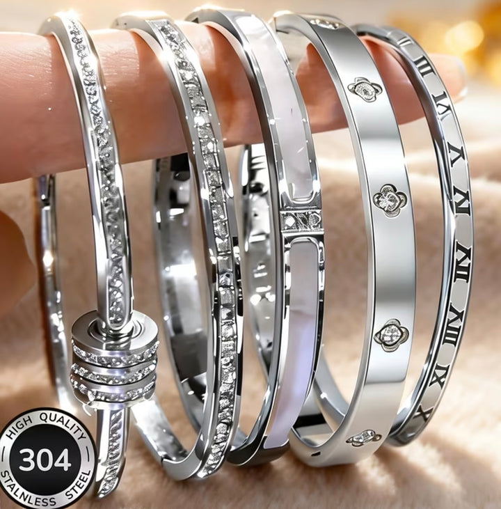 Five-piece silver-tone bangle bracelet set with crystal detailing, Roman numeral accents and clover design stacked on wrist.