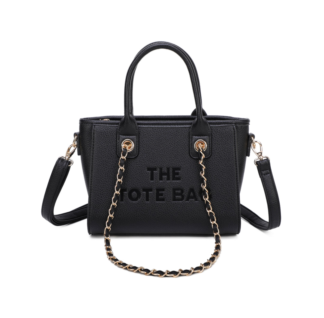 A black tote bag with a chain handle, featuring a front zipper pocket and gold tone metal hardware. The ‘THE TOTE BAG&