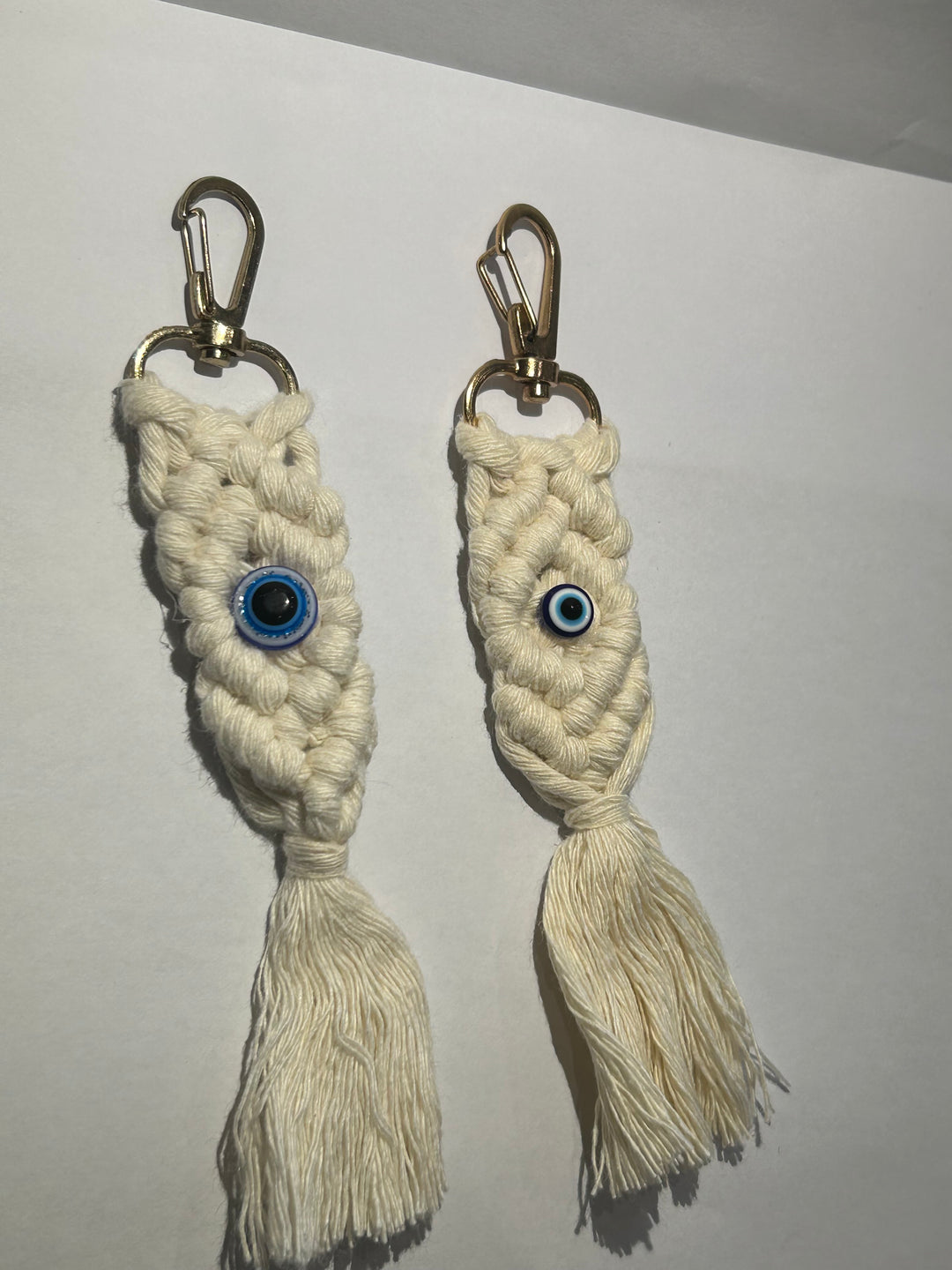 A pair of key rings with a blue eye design, made of a woven beige material