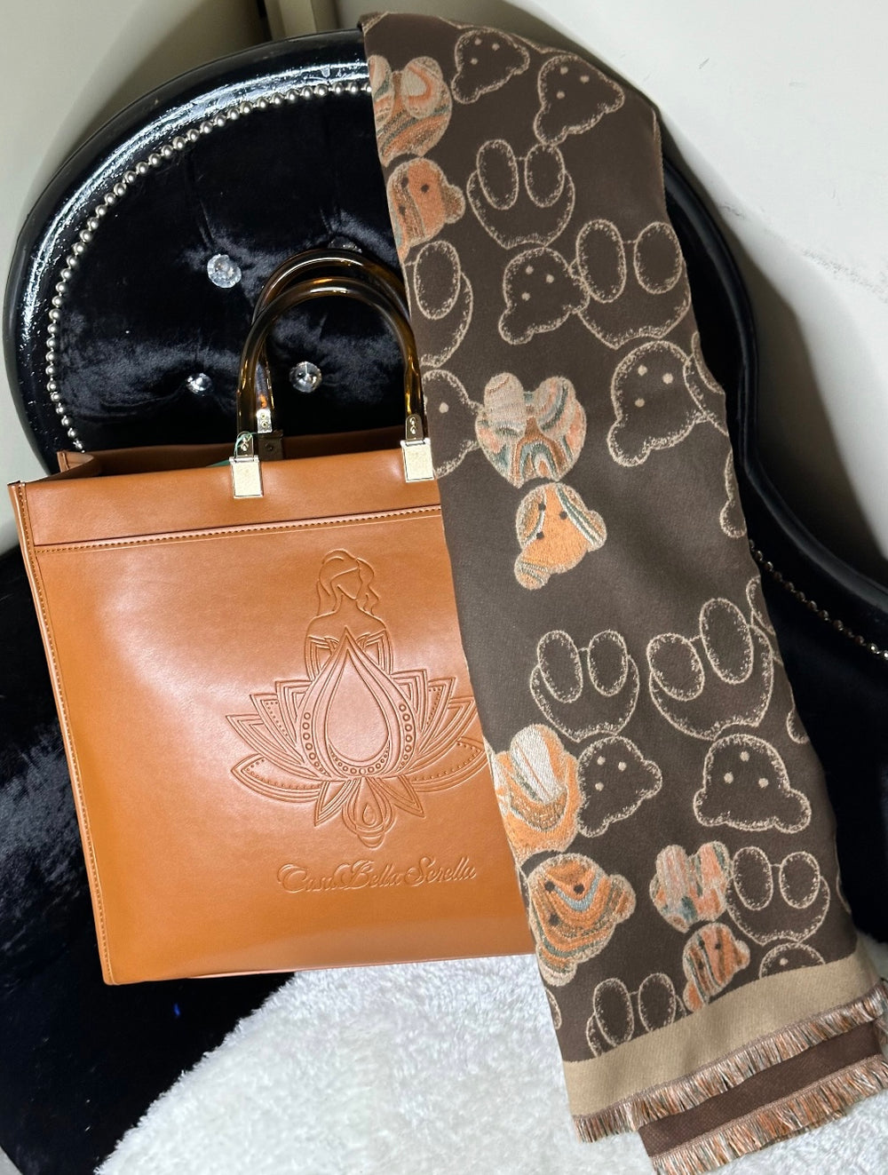 An image showing a tan handbag tote with an embossed cbs logo design, and a scarf. 