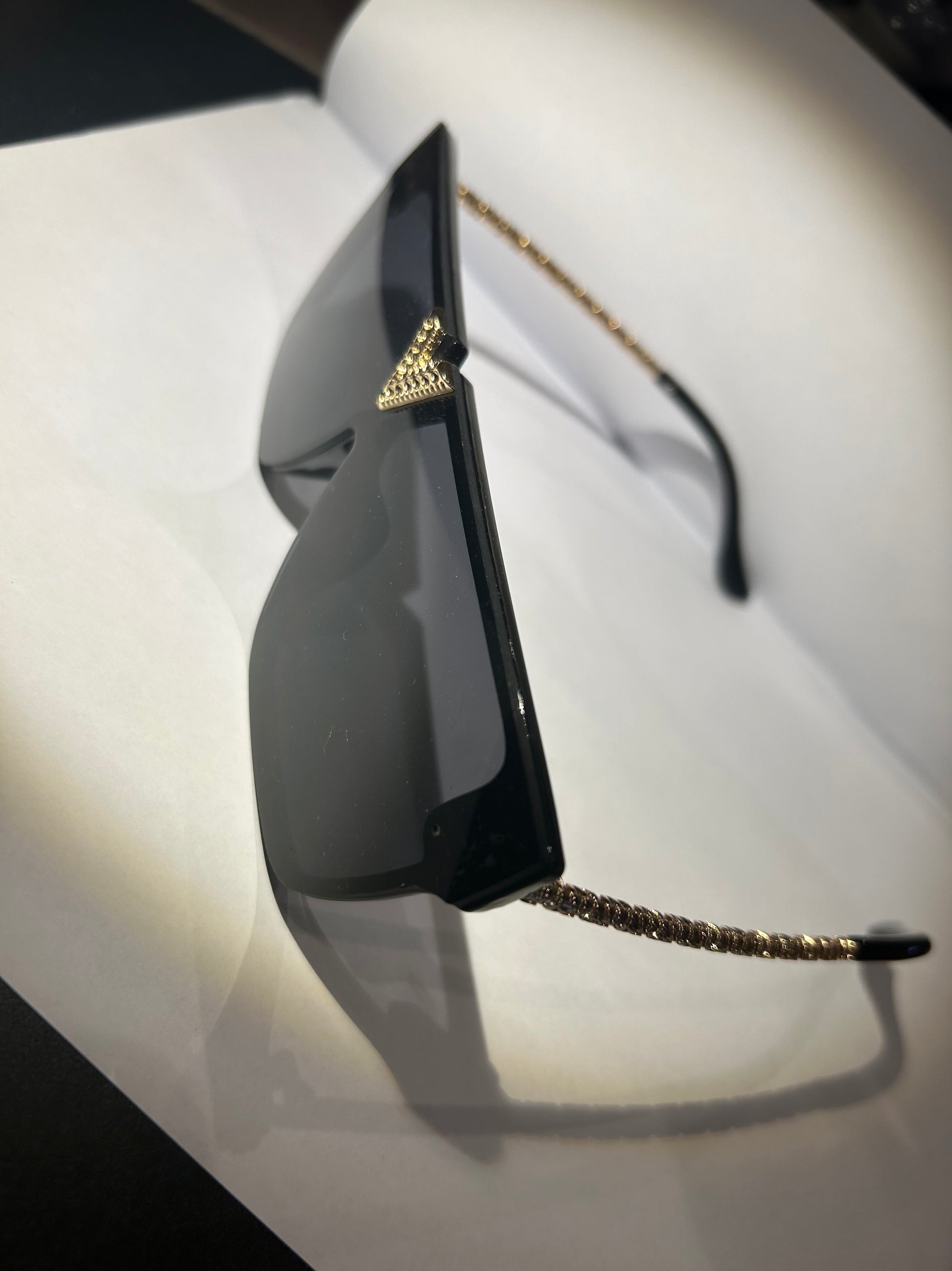 A pair of black sunglasses with gold detailing on the arms.