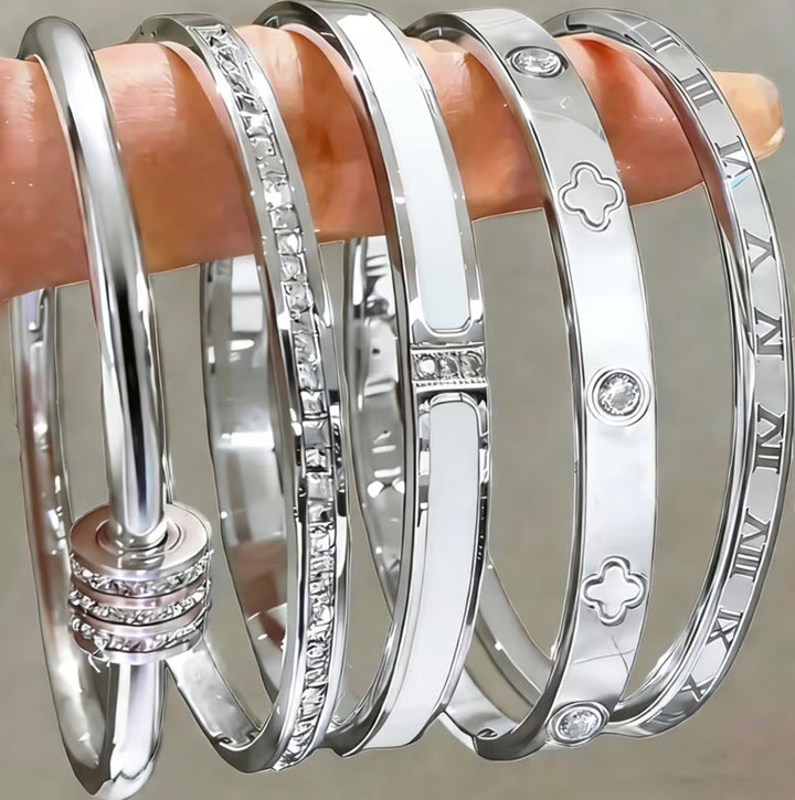 Five-piece silver-tone bangle bracelet set with crystal detailing, Roman numeral accents and clover design stacked on wrist.