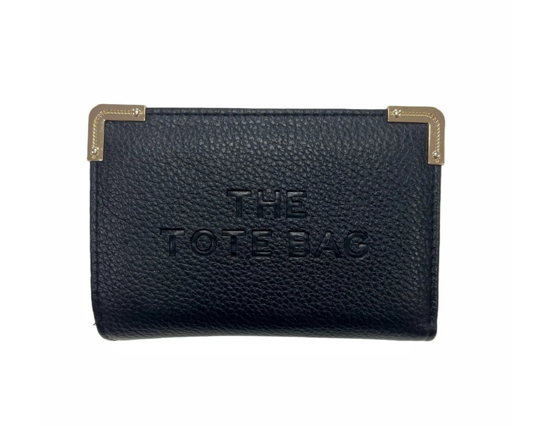 A black synthetic tote bag with gold tone metal hardware, featuring a fold-over top with a closure, and the THE TOTE BAG' embossed on the front.