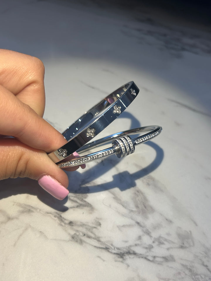 Two silver bracelets- one featuring screw-style detailing and the other with sparkling crystal embellishments and a wrap-around nail-inspired design.