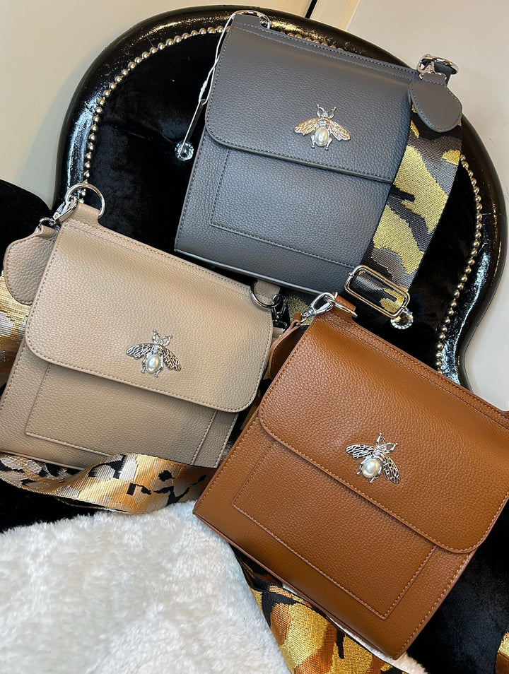 A beige, tan and grey  satchel crossbody bag with a bee design on the front flap, featuring a camouflage pattern on the strap.