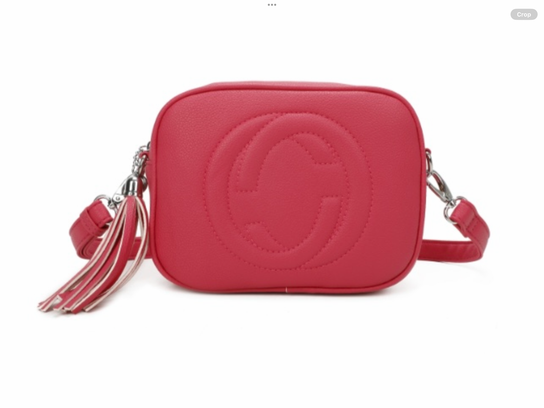A pink crossbody camera bag with embossed circle logo design, detachable strap and tassel zip detail