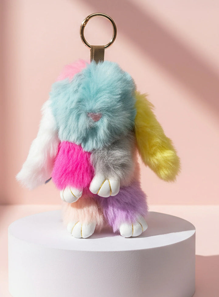 Multicolored fluffy keychain on a white pedestal with a pink background