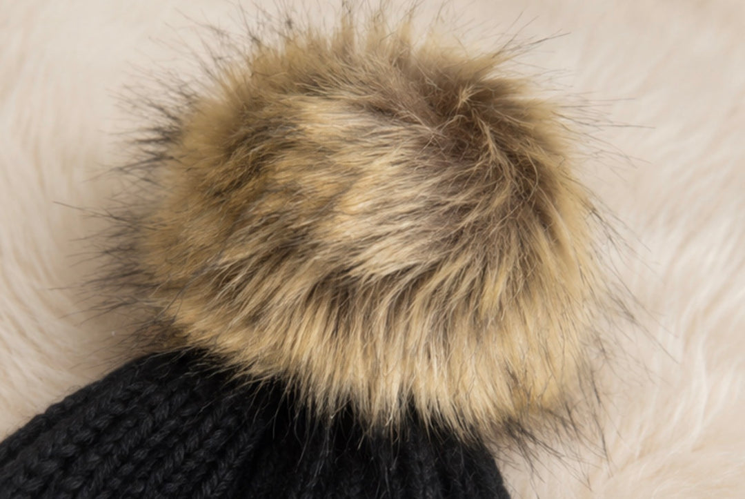 Children’s black ribbed knit bobble hat with a large beige faux fur pom pom