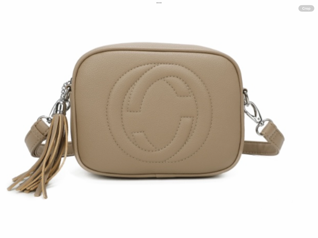 A beige crossbody camera bag with embossed circle logo design, detachable strap and tassel zip detail
