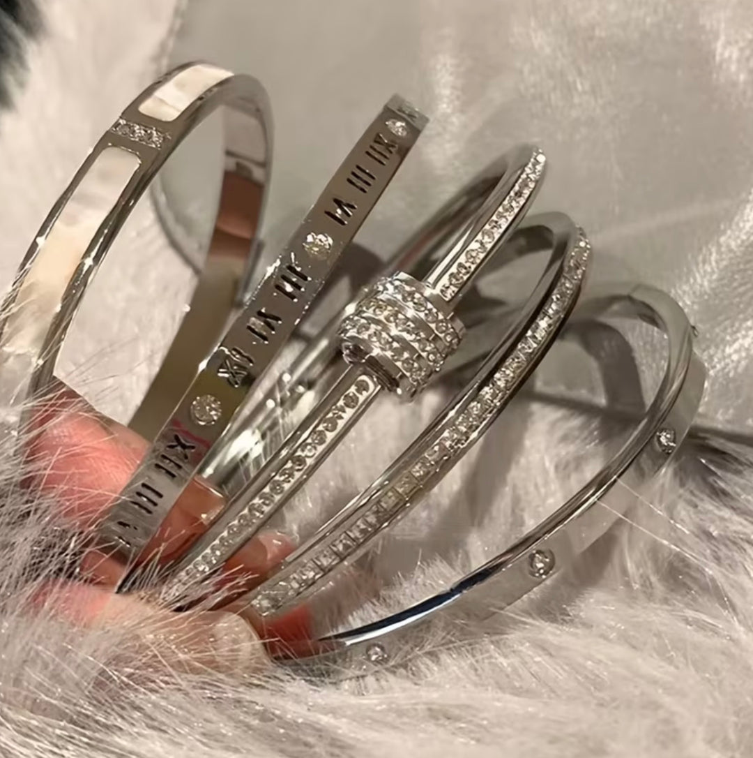 Five-piece silver-tone bangle bracelet set with crystal detailing, Roman numeral accents and clover design stacked on wrist.