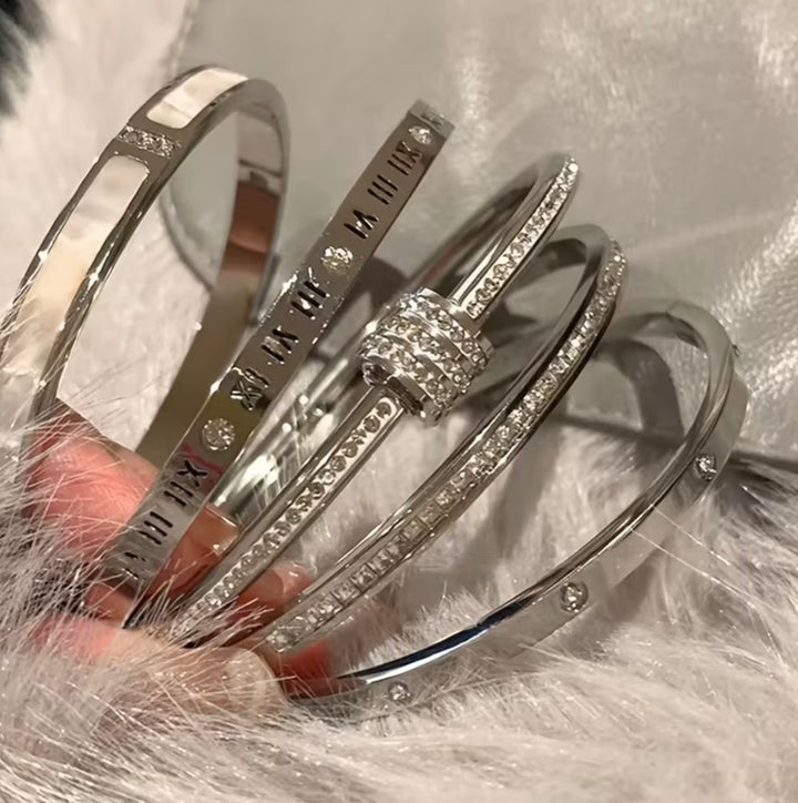 Five-piece silver-tone bangle bracelet set with crystal detailing, Roman numeral accents and clover design stacked on wrist.