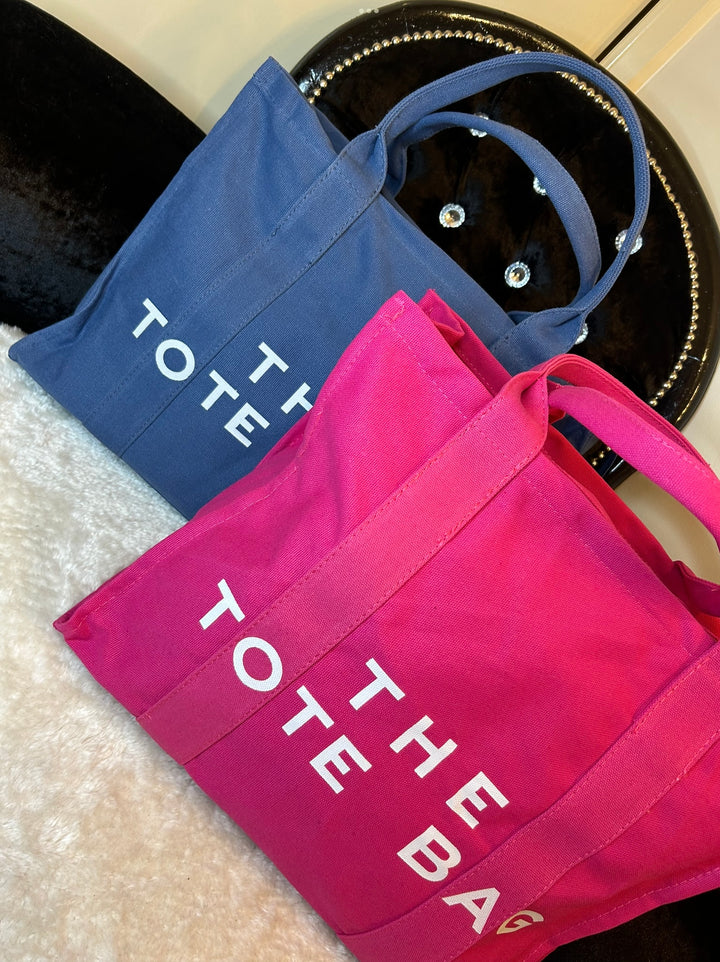 Two canvas tote bags, one in pink and the other in blue, both with the text &
