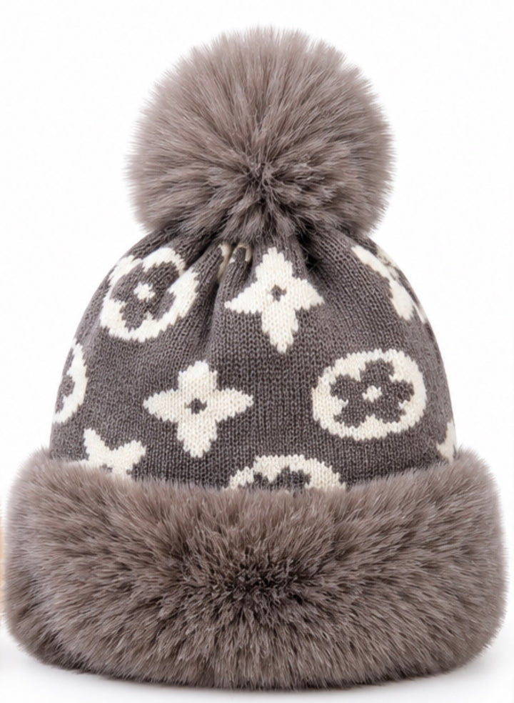 Luxury knitted winter bobble hats in camel beige and grey with cream monogram-style pattern, oversized fluffy pom poms, thick faux fur trims and soft fleece lining.