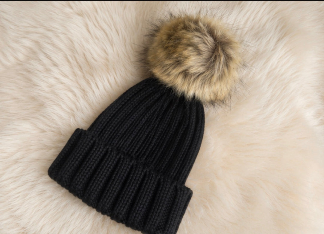 Children’s black ribbed knit bobble hat with a large beige faux fur pom pom