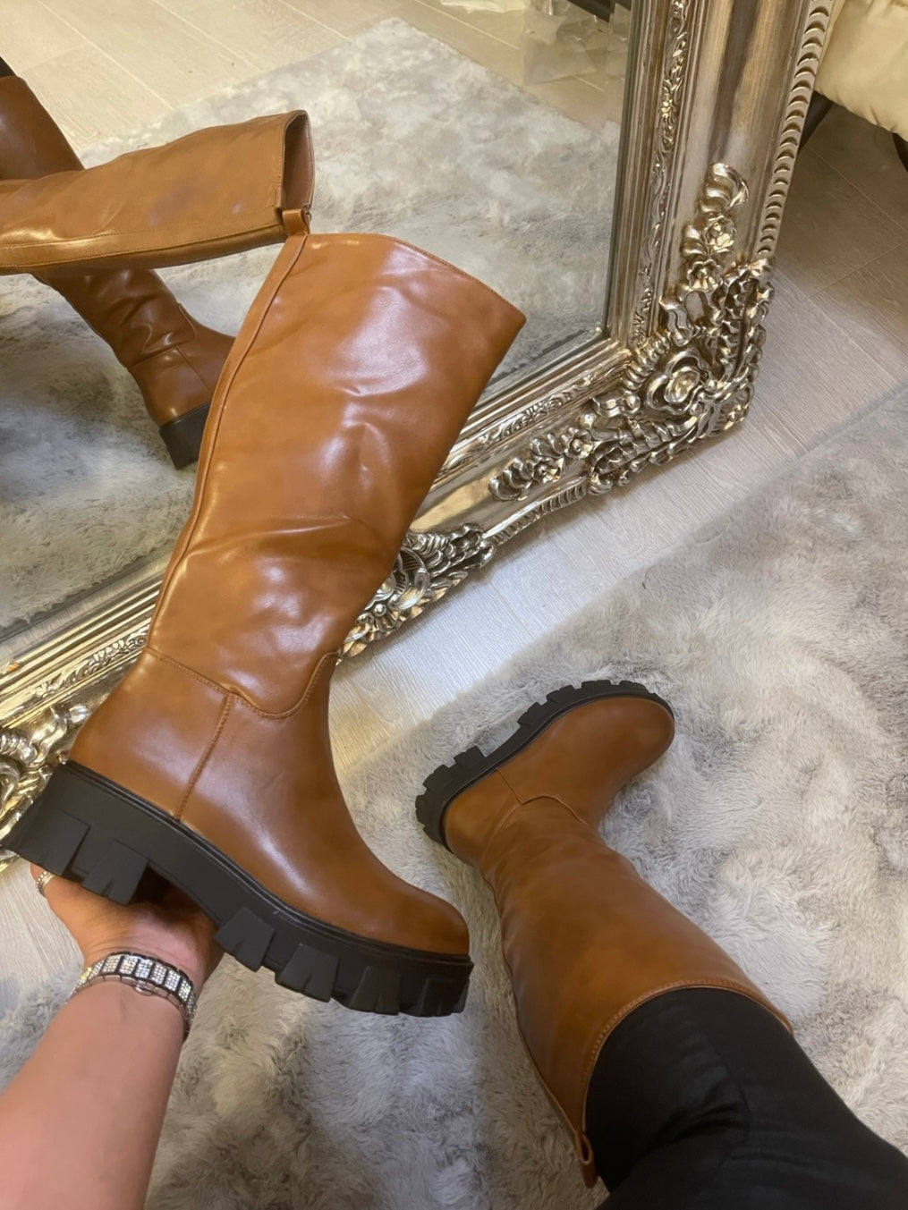 Tan knee high boots with black sole worn on feet, stylish women’s autumn footwear