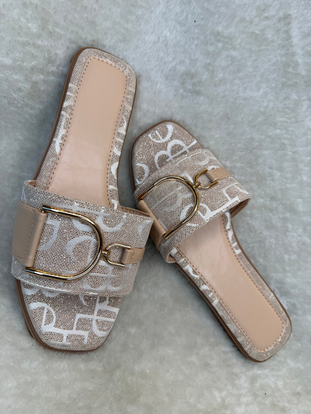 Rose gold monogram sliders with buckle detail displayed on neutral background