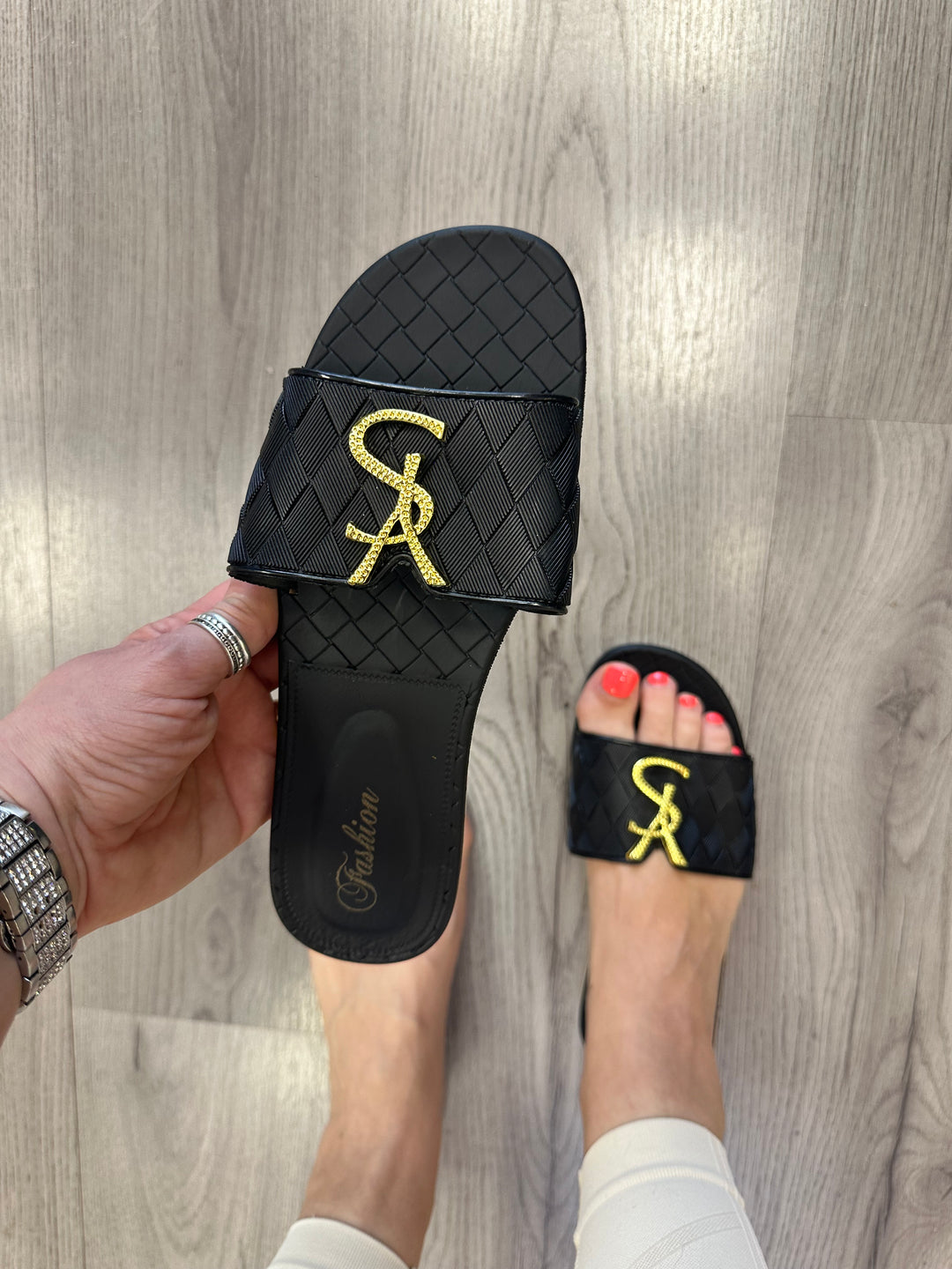 Black jelly sliders with gold letter details on them.