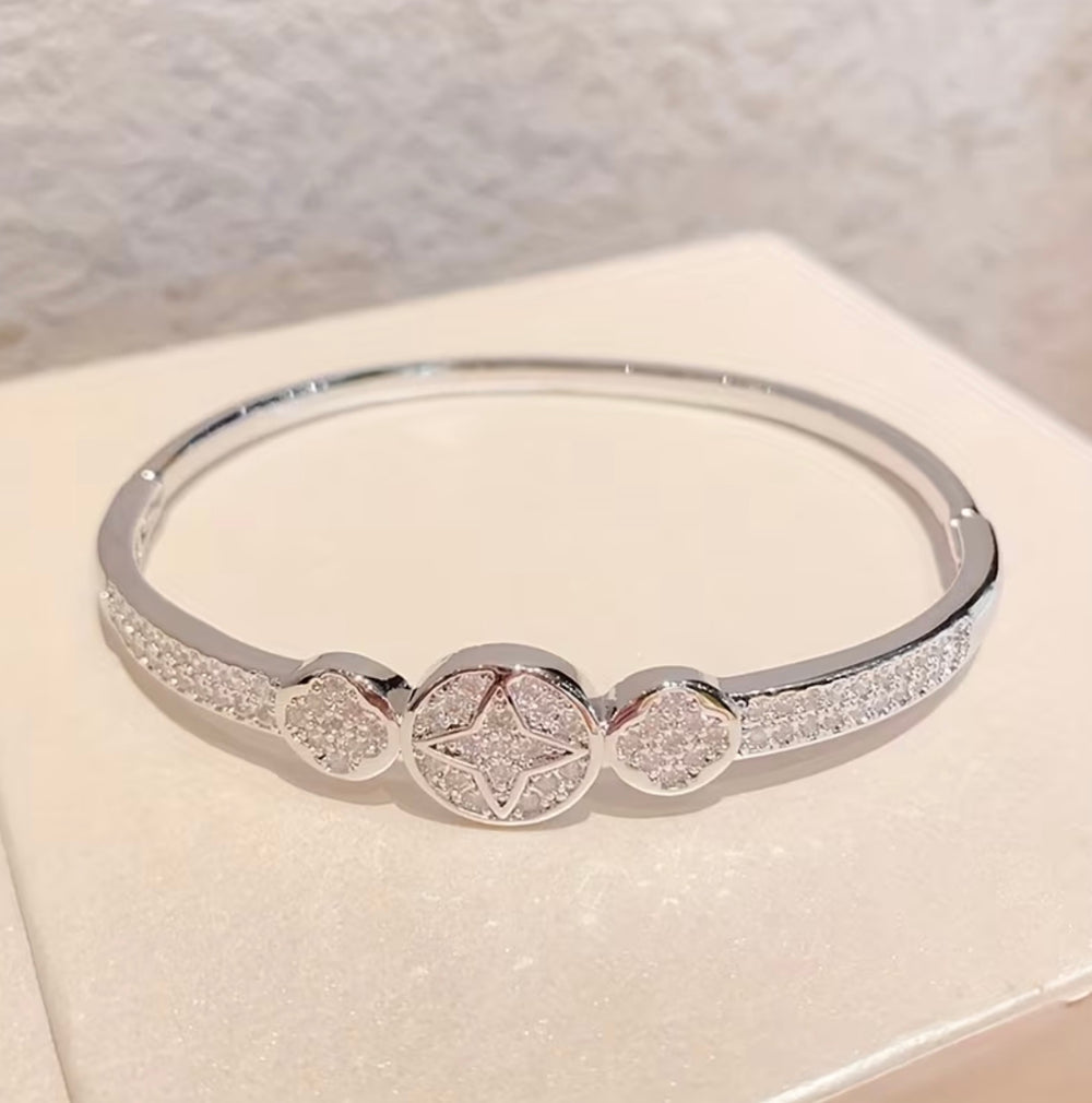 Silver crystal bangle bracelet with sparkling star and heart detail design on a silver-tone hinged cuff bracelet.