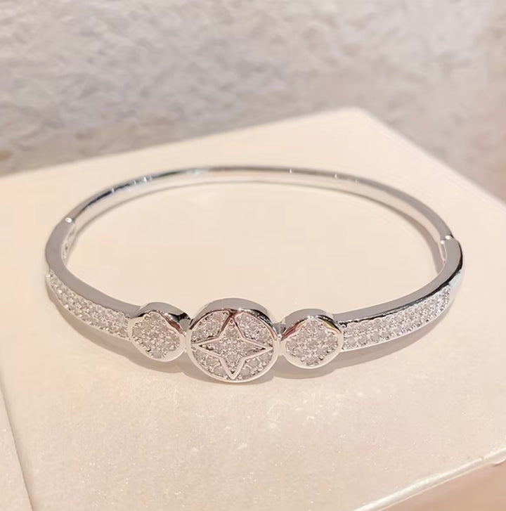 Silver crystal bangle bracelet with sparkling star and heart detail design on a silver-tone hinged cuff bracelet.