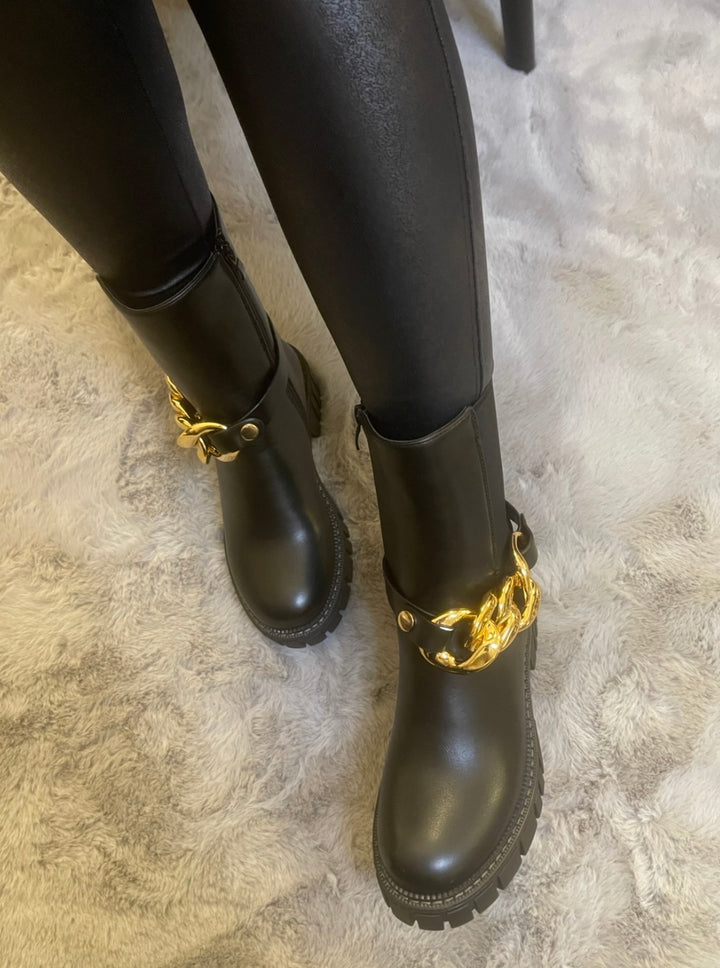 Black chunky ankle boots with gold chain detail worn on feet, stylish women’s boots
