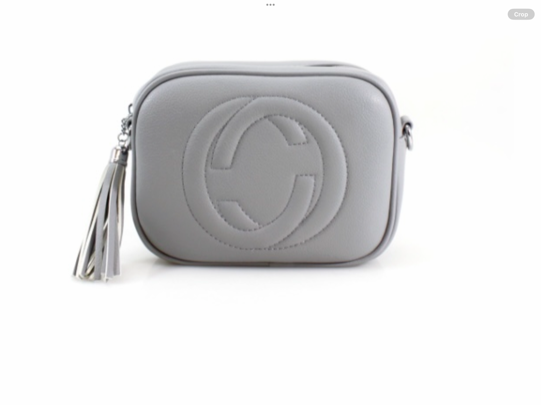 A grey crossbody camera bag with embossed circle logo design, detachable strap and tassel zip detail