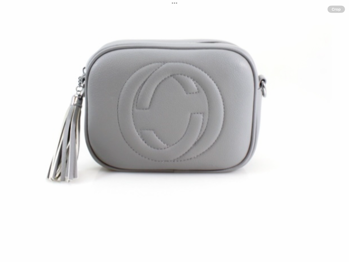 A grey crossbody camera bag with embossed circle logo design, detachable strap and tassel zip detail
