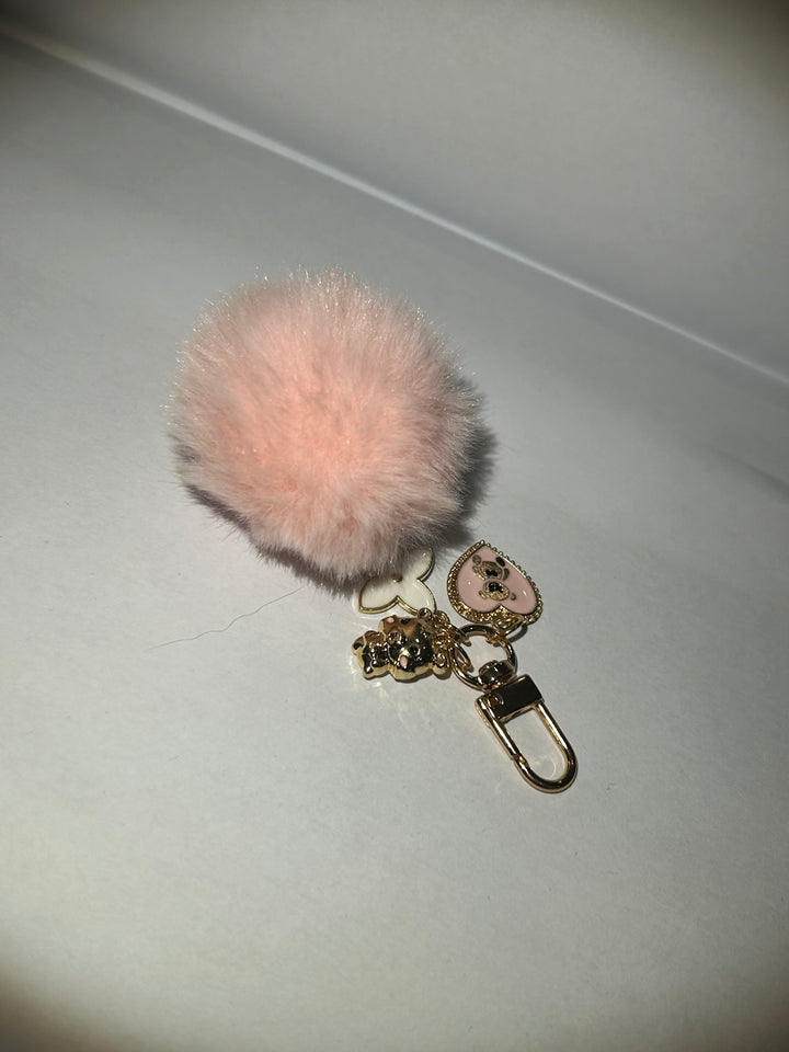 A pink clover flower key ring with a fluffy pom-pom and additional charms attached to it.