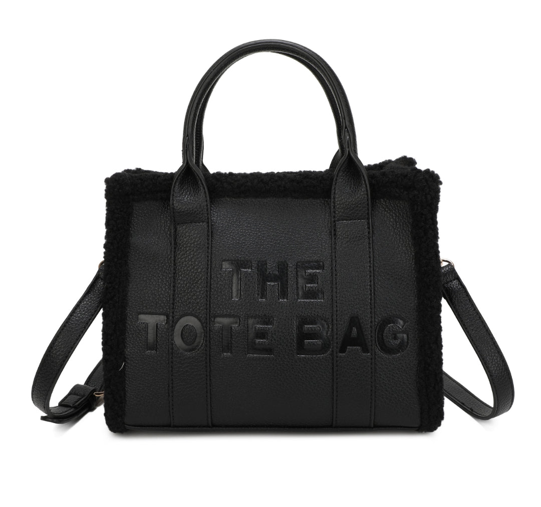 Tote bags with fuzzy edge trim, embossed with ‘The Tote Bag’ on the front in black 