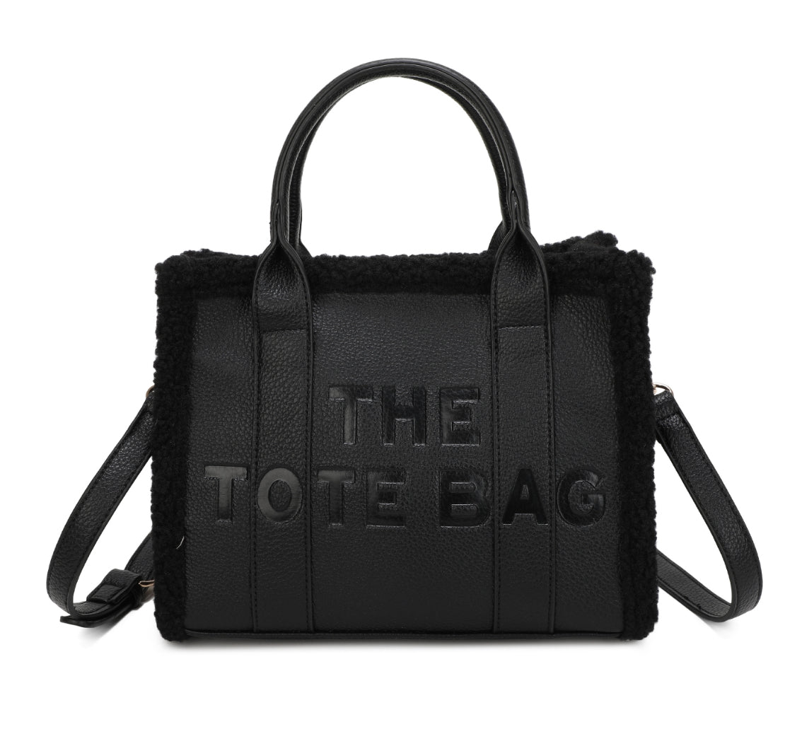 Tote bags with fuzzy edge trim, embossed with ‘The Tote Bag’ on the front in black 