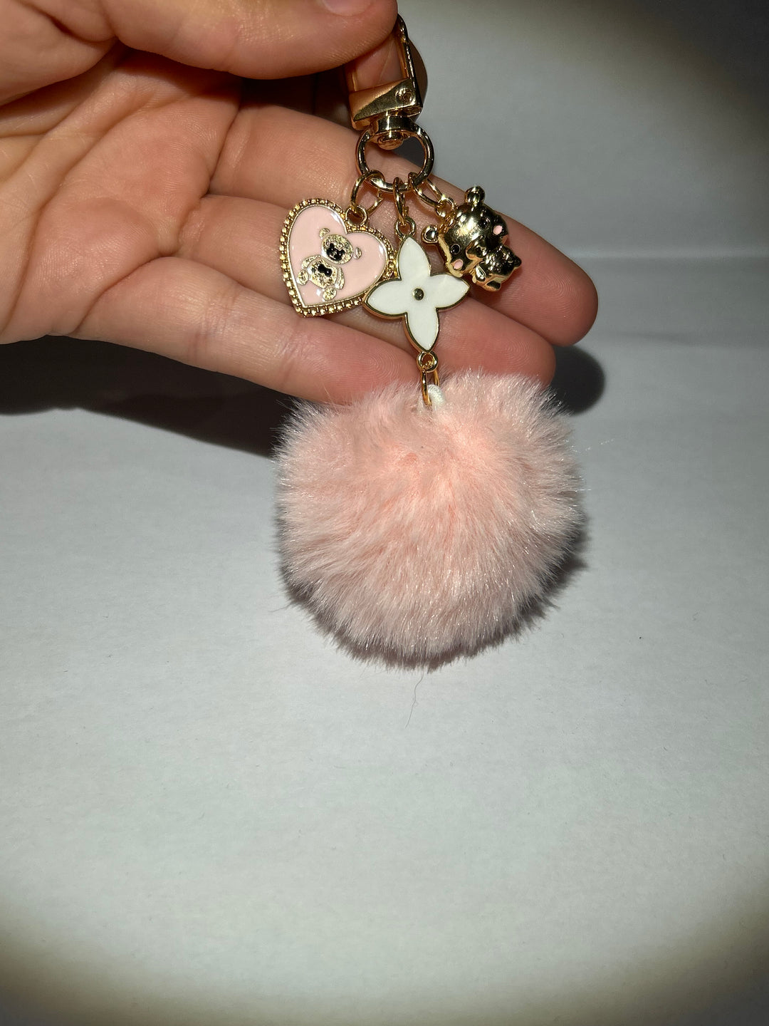 A pink clover flower key ring with a fluffy pom-pom and additional charms attached to it.