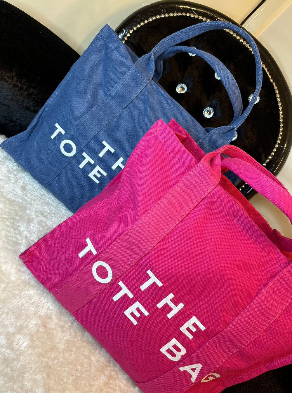 Two canvas tote bags, one in pink and the other in blue, both with the text 'THE TOTE BAG' printed on them.