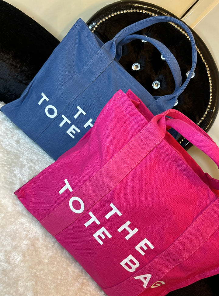 Two canvas tote bags, one in pink and the other in blue, both with the text &