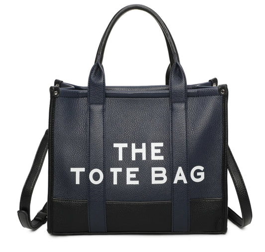 Two tone colour tote bag in navy. Black at the bottom of the bag, white writing stating “the tote bags” displaying a long strap to crossbody the bag.