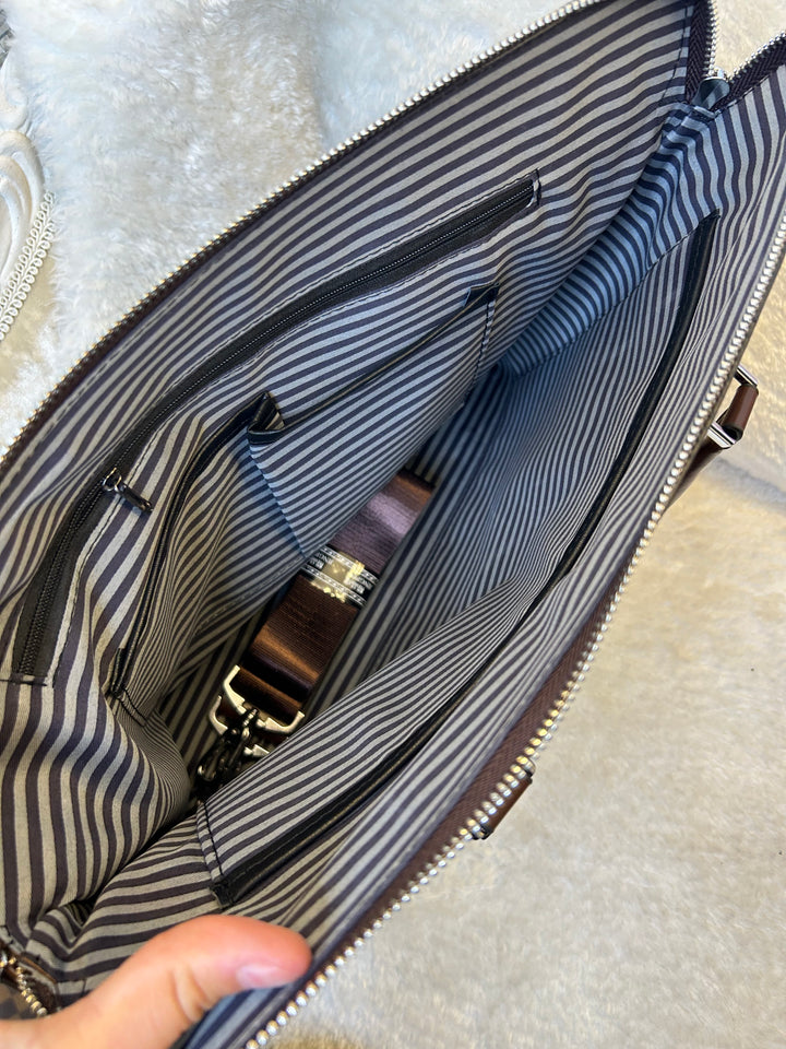 Close-up of a striped bag with a brown strap and gold buckle.
